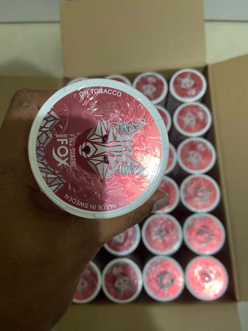 Container of White Fox tobacco with a box of similar containers in the background