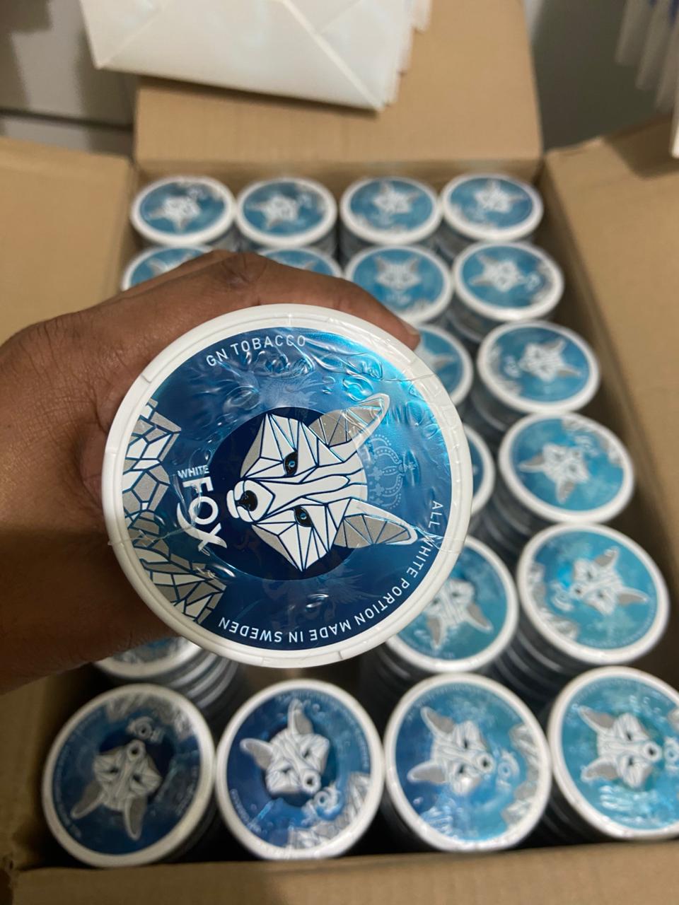 Hand holding a blue and white container with a brand logo, surrounded by more containers